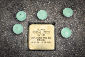 Botlatókő látható a járdába illesztve, körülötte mécsesekkel; a kő Rostás Jánosra emlékezik, akit 1944-ben deportáltak és 1945 januárjában megöltek.